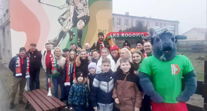 Koziołek LKS Rogowo z kibicami i zawodnikami na tle hokejowego muralu fot. nadesłane